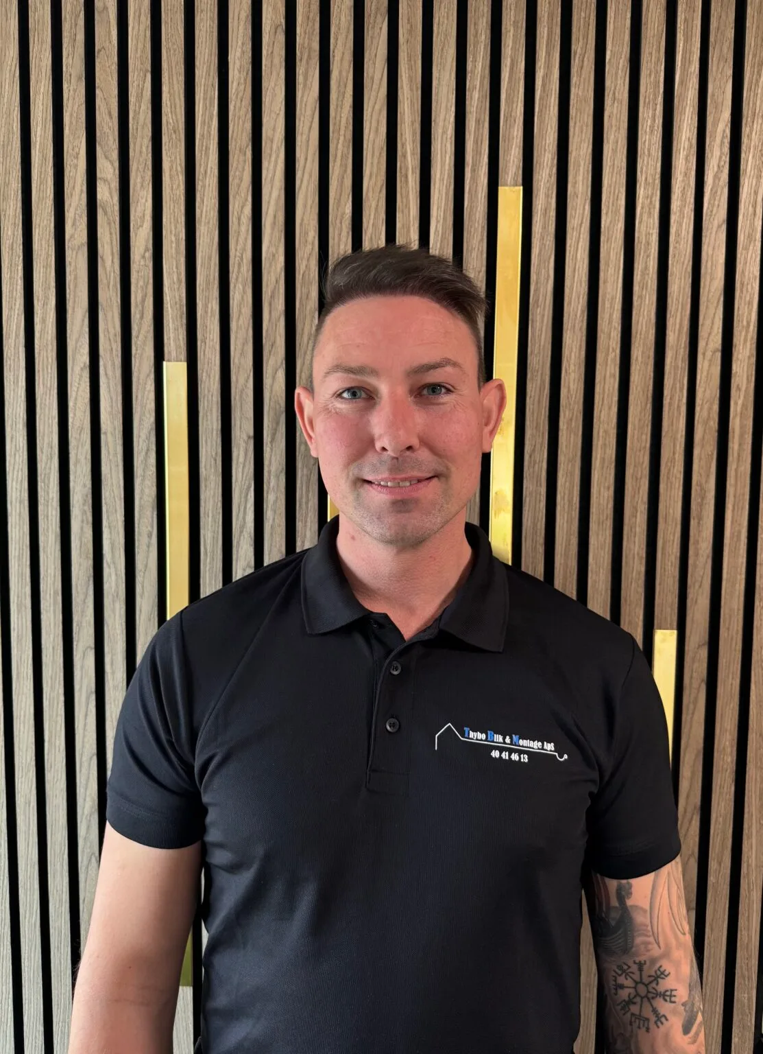Man in black polo shirt, wood backdrop.